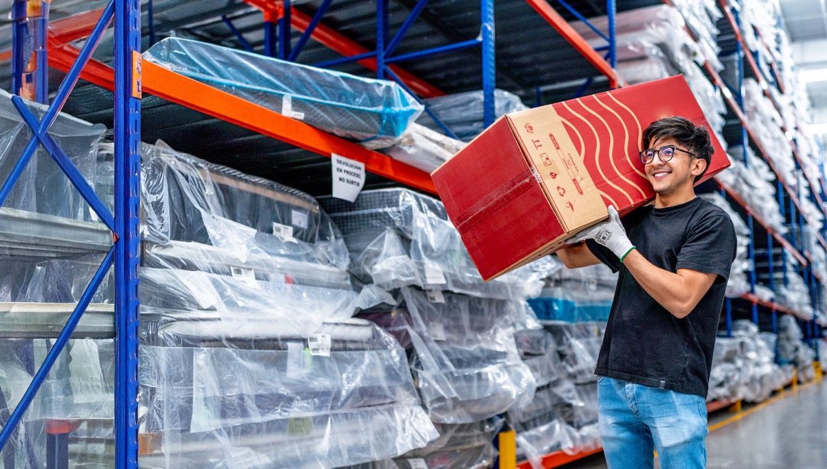 Warehouse worker carrying a box between tall storage racks